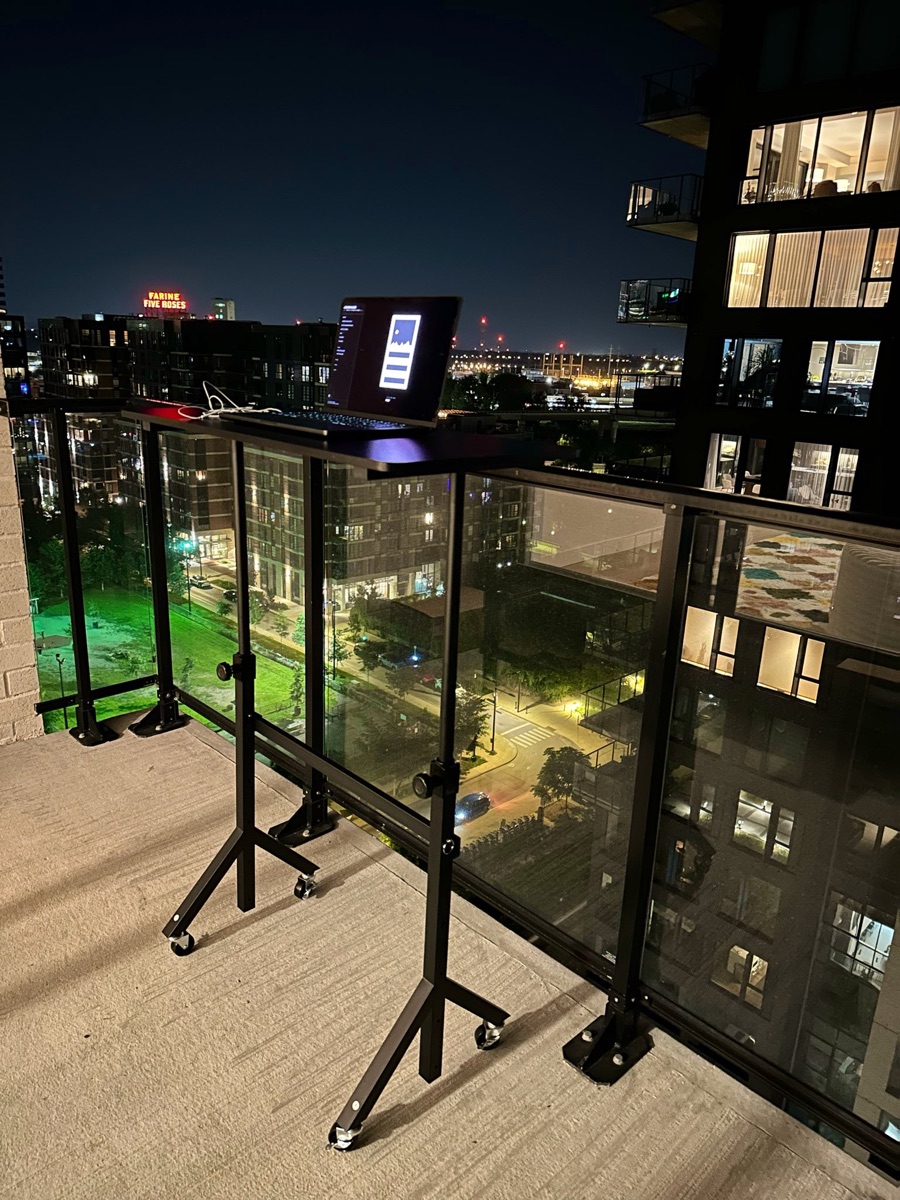Laptop on a standing desk on a Montreal balcony at night, with the Farine Five Roses sign in the distance